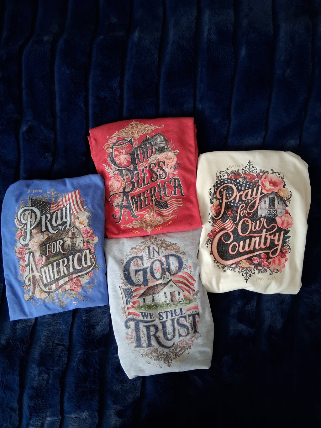 Four t-shirts with patriotic designs on a dark fabric background